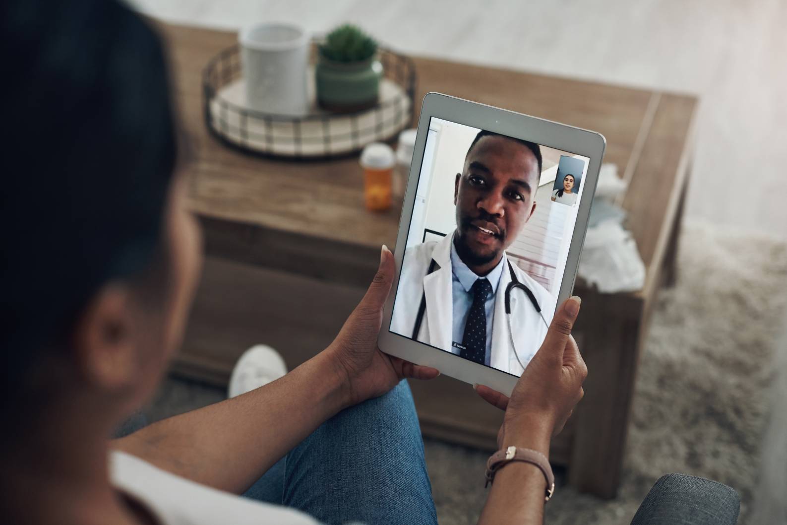 Person video calling a doctor on a tablet, with a table and items in the background.