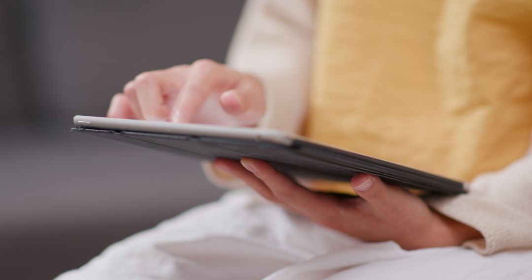 Person using a tablet, holding it with one hand and touching the screen with the other; yellow garment in the background.