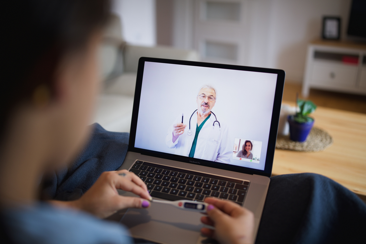 Young female is having video call with her male doctor checking her temperature while social distancing and quarantine