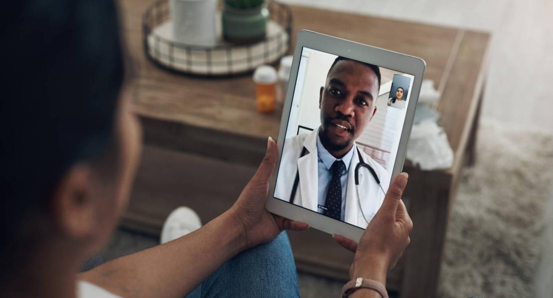 Person video calling a doctor on a tablet, with a table and items in the background.