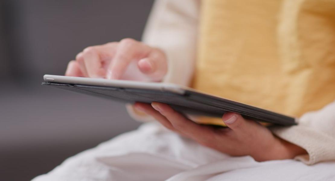 Person using a tablet, holding it with one hand and touching the screen with the other; yellow garment in the background.