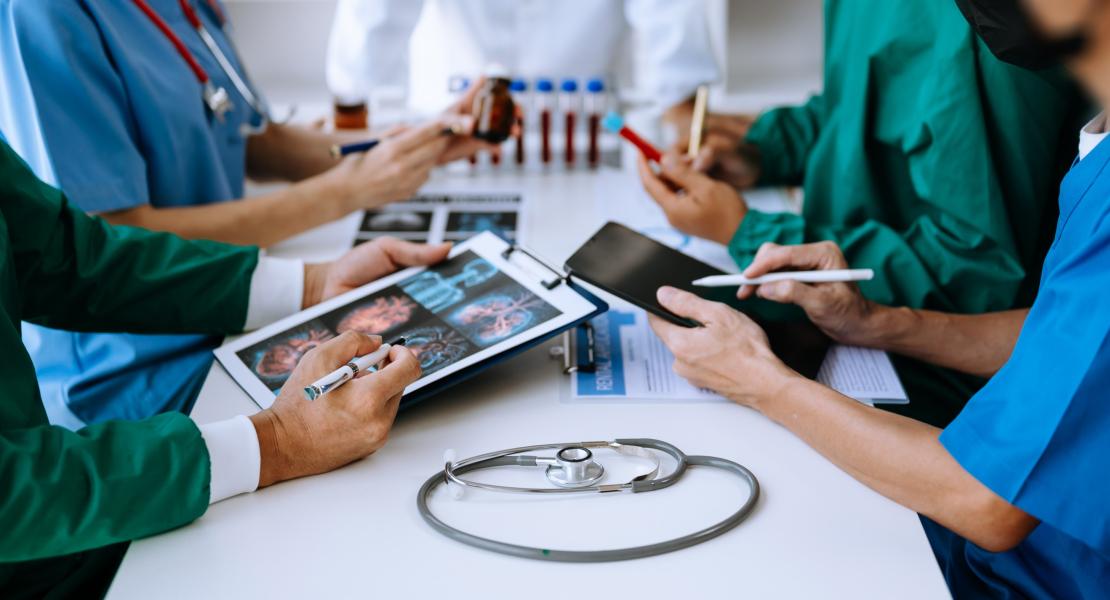 A team of healthcare professionals in scrubs collaborating around a table, reviewing medical scans on a clipboard and analyzing data on a tablet.
